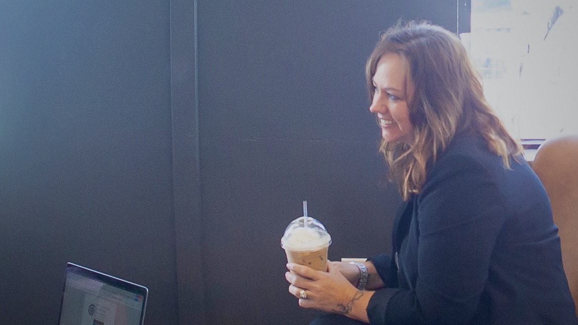 Woman smiling and holding an iced coffee during a client meeting in a café.