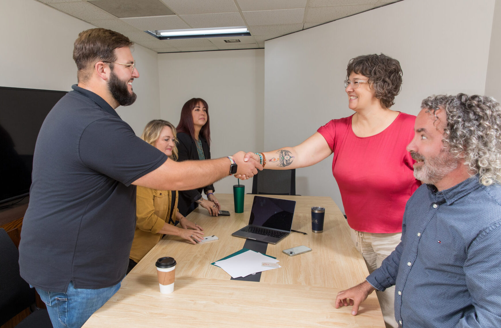 a group of professionals standing around a conference table while a woman and a man are shaking hands
